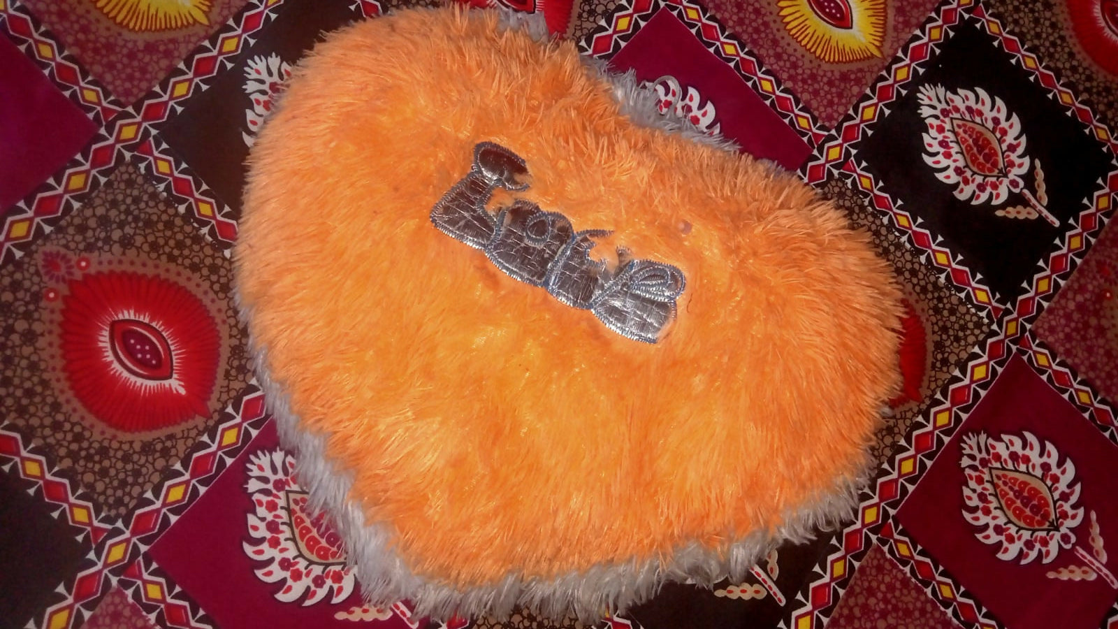 Orange fluffy object with a metal clip on a patterned fabric background