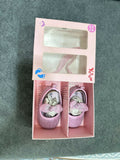 Pink baby shoes with floral design in a box on a gray background