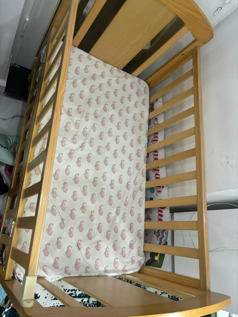 Wooden crib with a patterned mattress cover in a room setting.