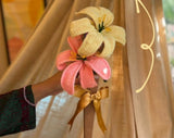 Decorative hair clip with pink and yellow flowers held by a hand against a curtain background