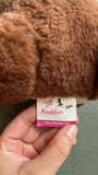 Hand holding a brown plush toy with a 'Soft Buddies' label.