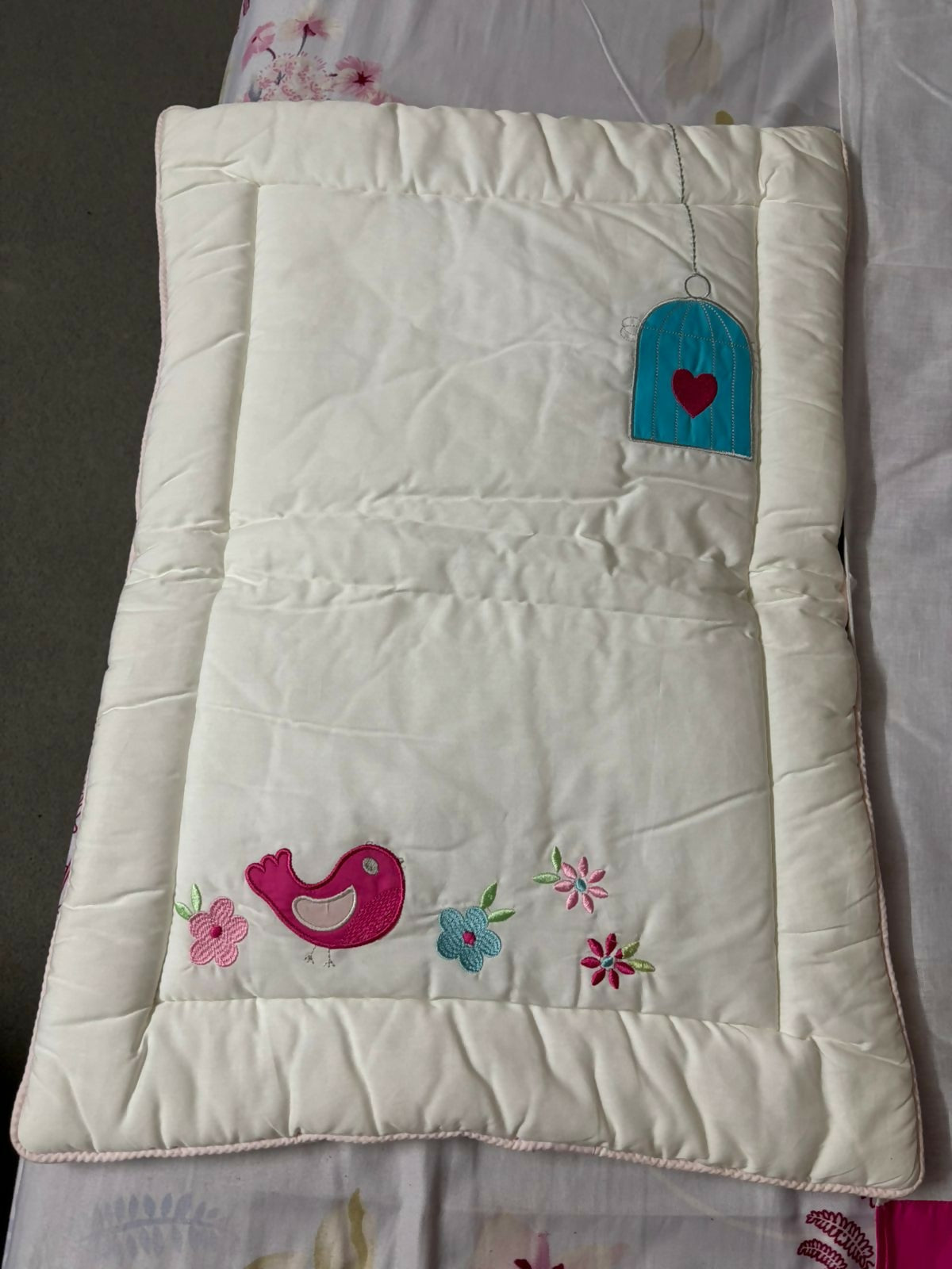White quilt with embroidered designs on a floral fabric background