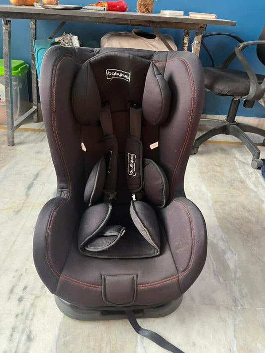 Brown and black car seat on a marble floor with a blue wall and metal table in the background.
