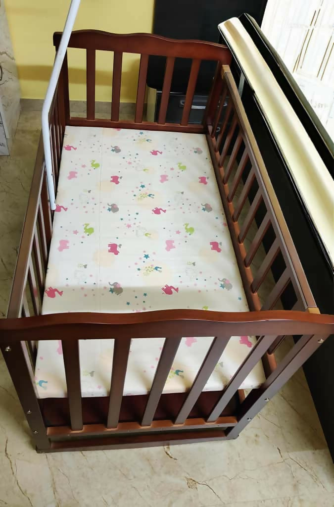 Wooden crib with a colorful mattress cover on a tiled floor.