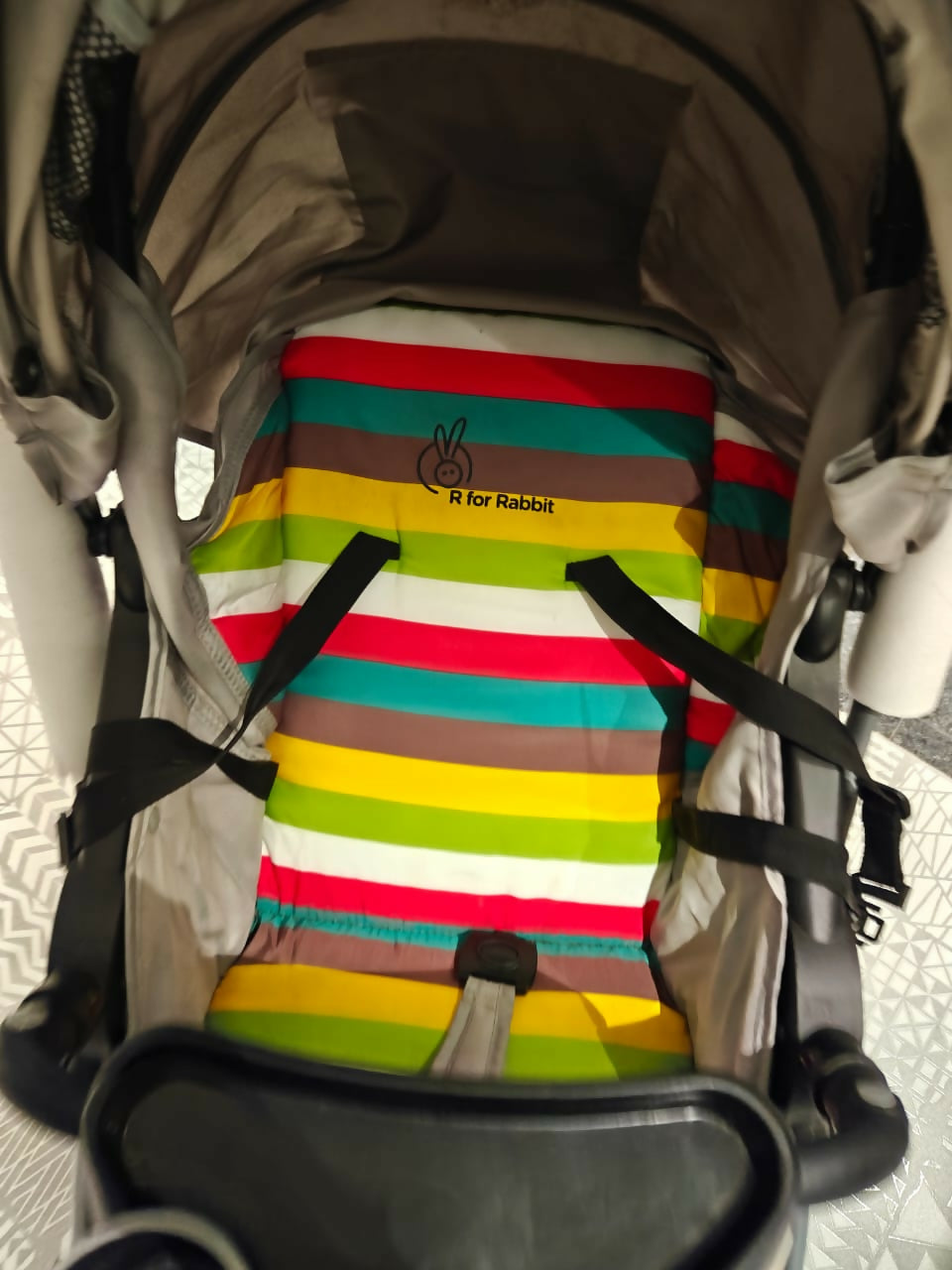 Colorful striped baby seat cover with 'R for Rabbit' logo on a stroller.