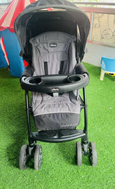 Gray and black stroller on a green surface with colorful background