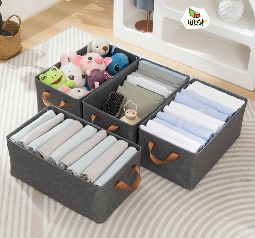 Gray storage boxes with handles containing folded clothes and toys on a bed.