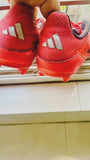 Red Adidas shoes with cleats on a tiled floor