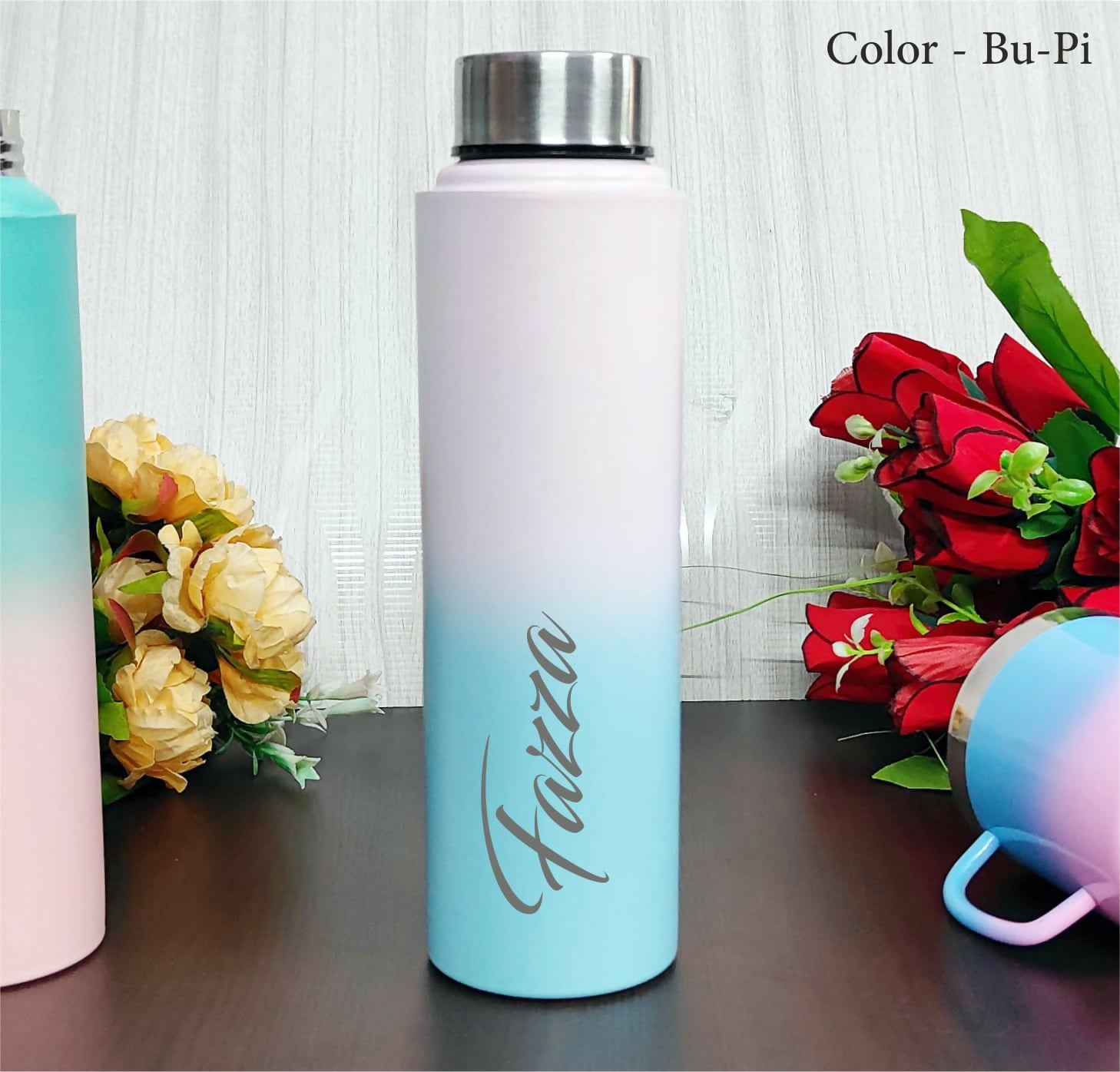 Gradient water bottle with 'Faizza' branding on a wooden surface with flowers.