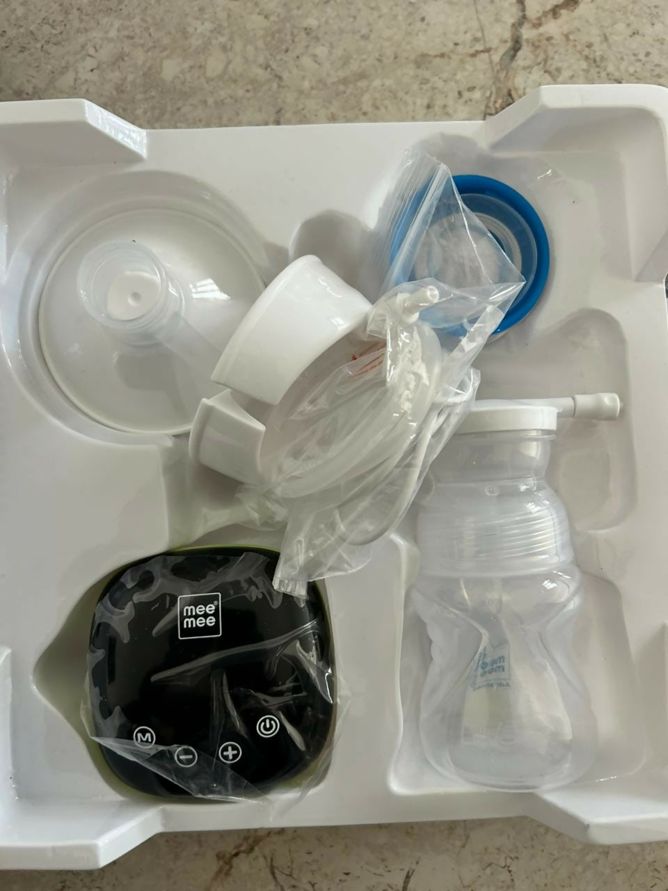 Breast pump and accessories in a white packaging tray on a concrete floor.