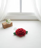 Red rose-shaped keychain on a white surface with a 'handmade with love' sign in the background.