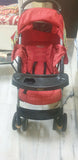 Red stroller with a black tray on a marble floor.