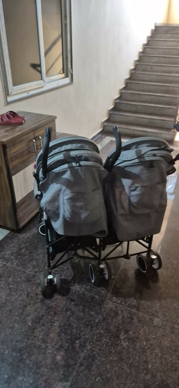 Two gray bags on wheels in a room with a staircase and wooden desk.
