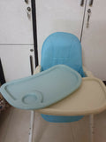 Children's high chair with blue cushion and beige tray against a white wall.
