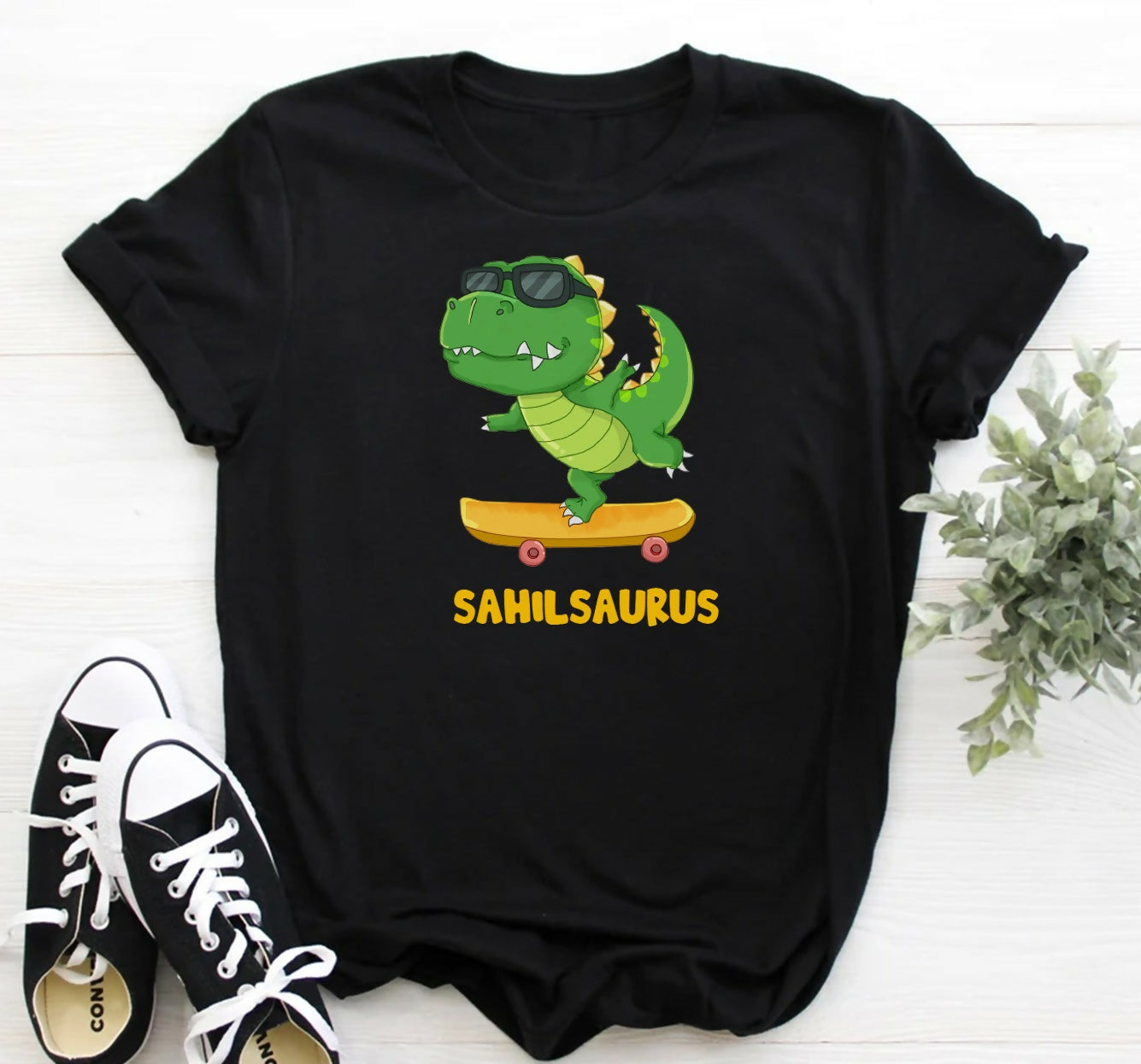 Black t-shirt with a cartoon dinosaur on a skateboard and 'Sahilsaurus' text, paired with black and white sneakers.
