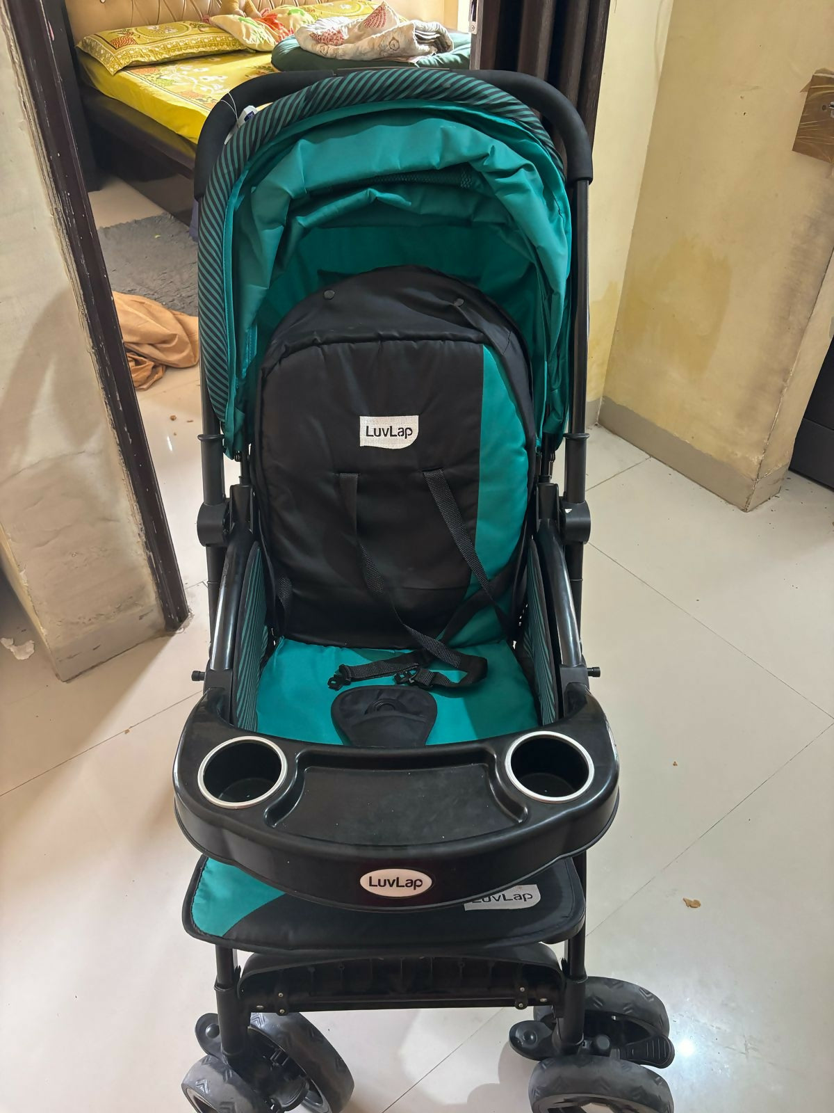 Green and black stroller with cup holders on a tiled floor.