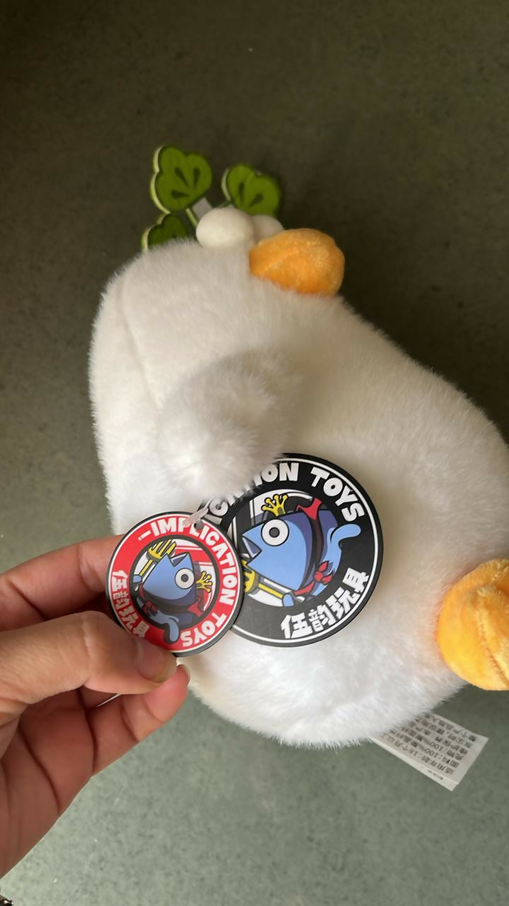 White plush toy with two badges held by a hand on a neutral background