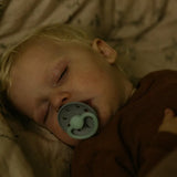 Child sleeping with a pacifier in a dimly lit setting