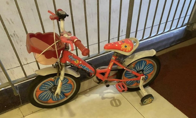 Children's bicycle with pink seat and basket on a tiled floor.