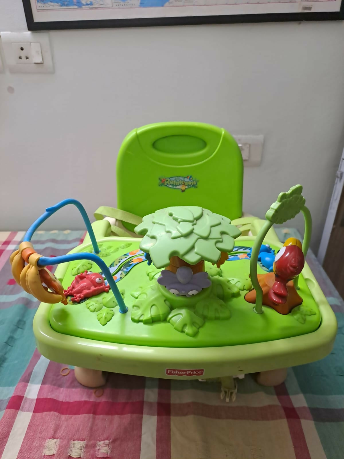 Green baby activity center with colorful toys on a checkered blanket.