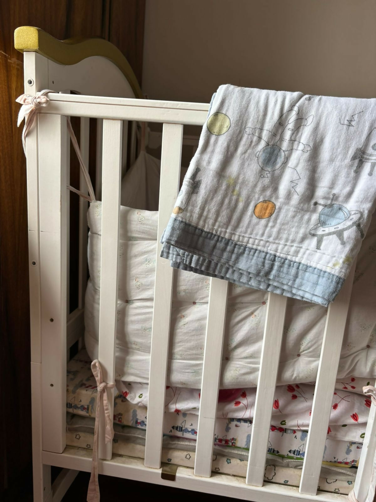 White crib with patterned bedding and a blanket draped over the top.