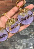 Hand holding personalized purple keychains with names 'Areesha', 'Neha', and 'Mania'.