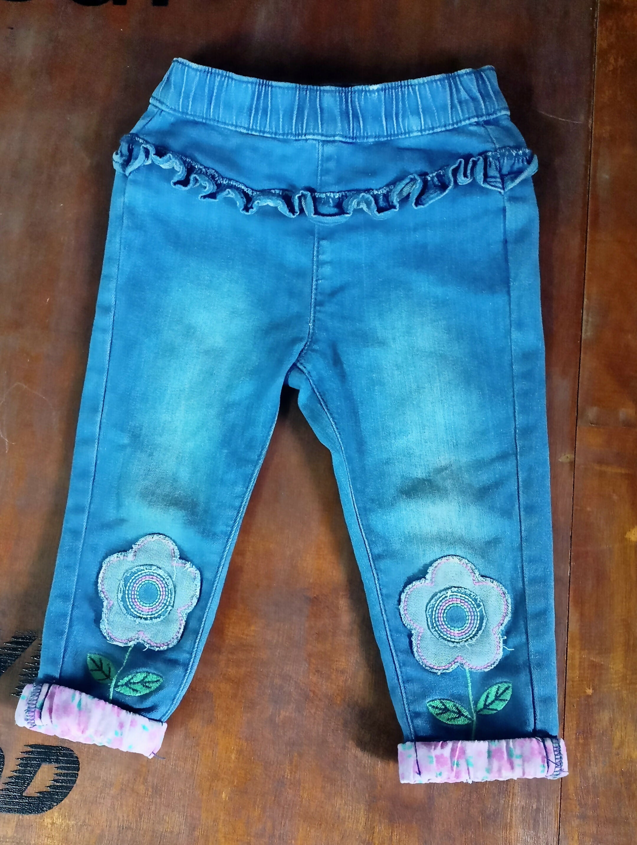Blue jeans with floral embroidery on a wooden surface
