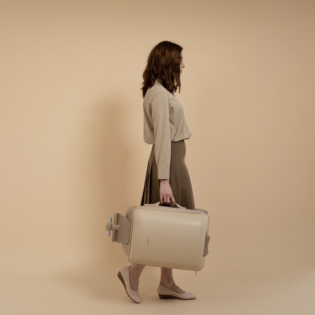Woman holding a beige suitcase against a beige background