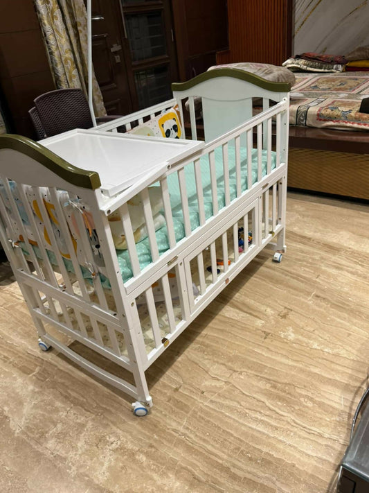 White crib with green trim on a wooden floor in a room.