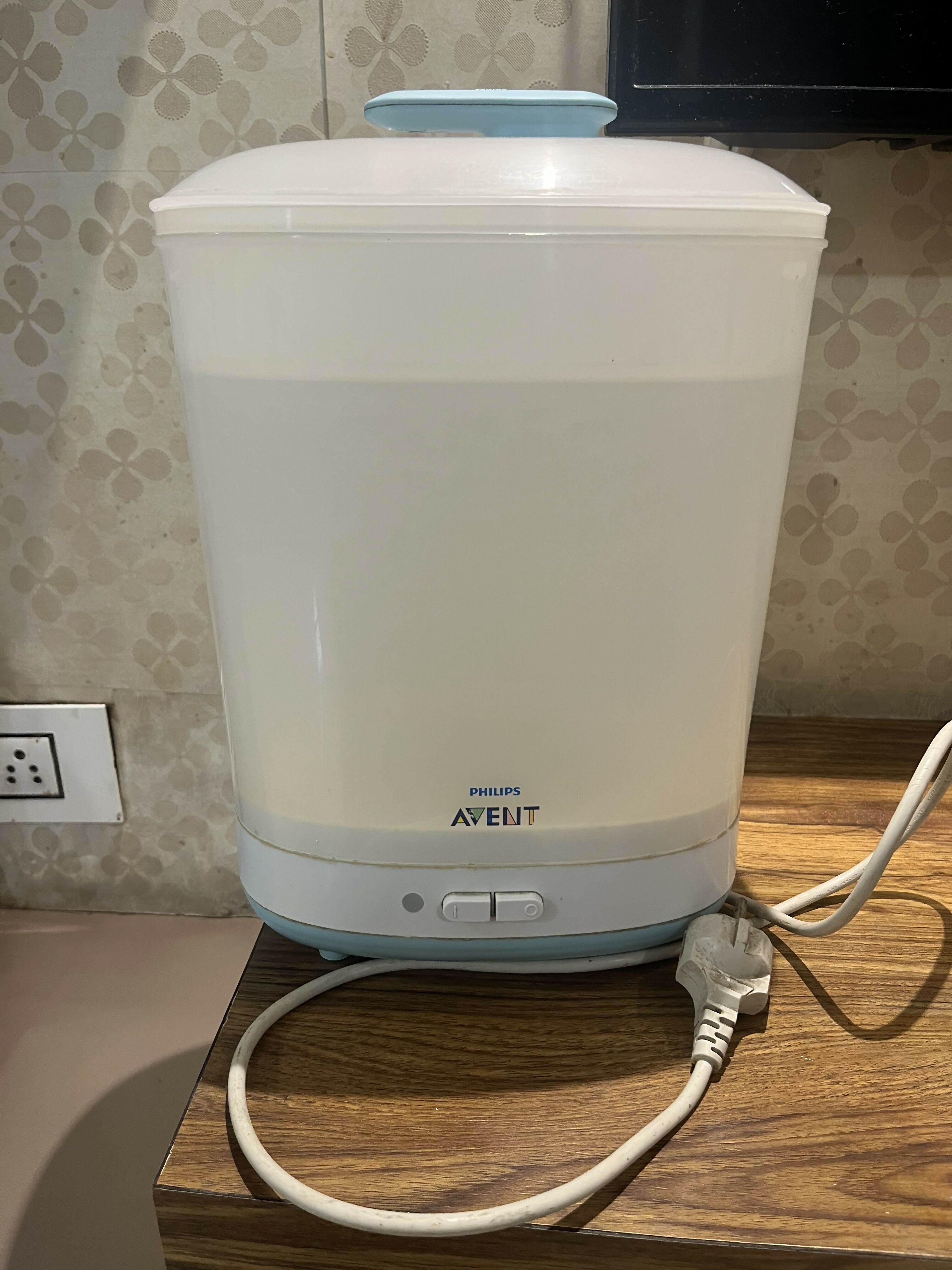 Philips Avent electric sterilizer on a wooden surface with a power cord plugged in.