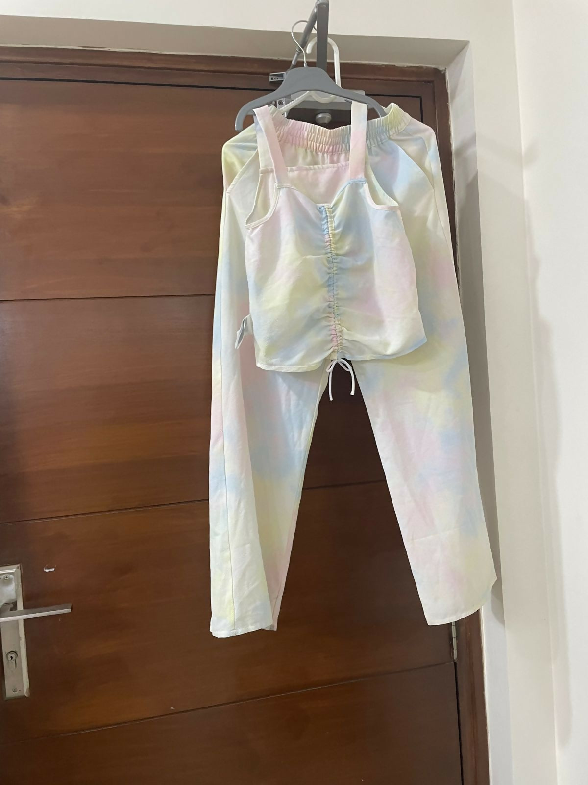 Colorful tie-dye outfit hanging on a hanger against a wooden door.
