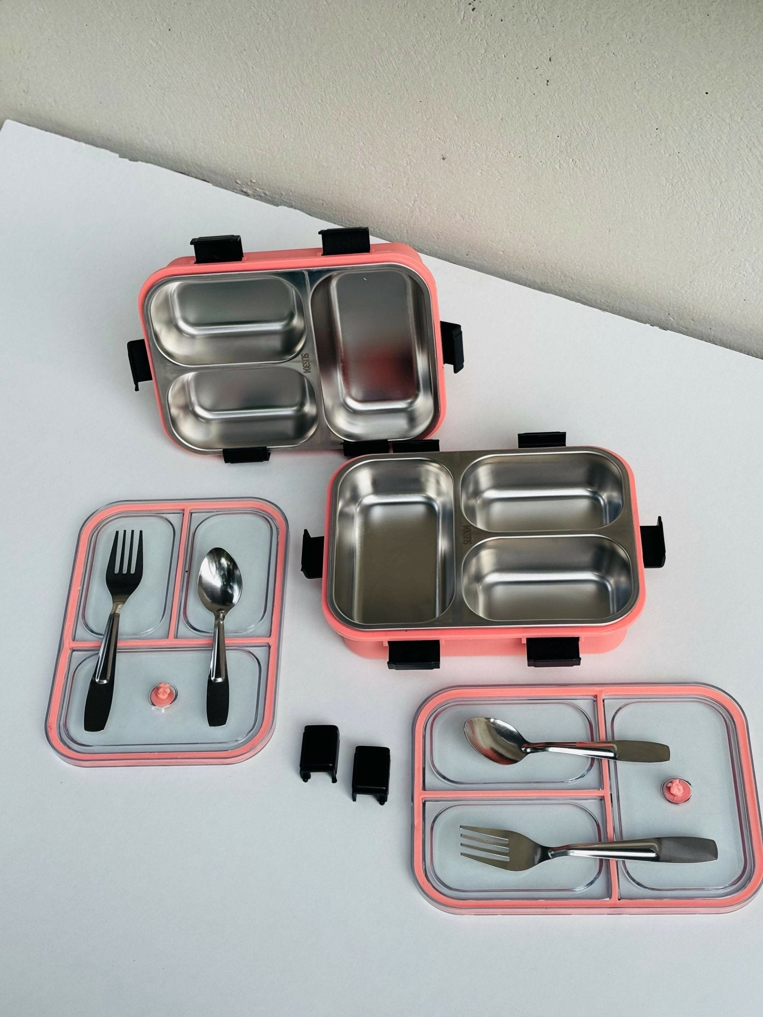 Stainless steel bento box with pink exterior and compartments, including utensils