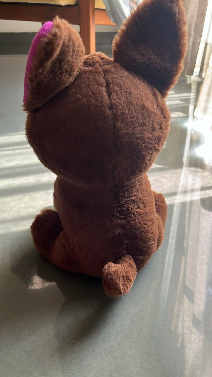 Brown plush toy with a pink bow on a reflective surface