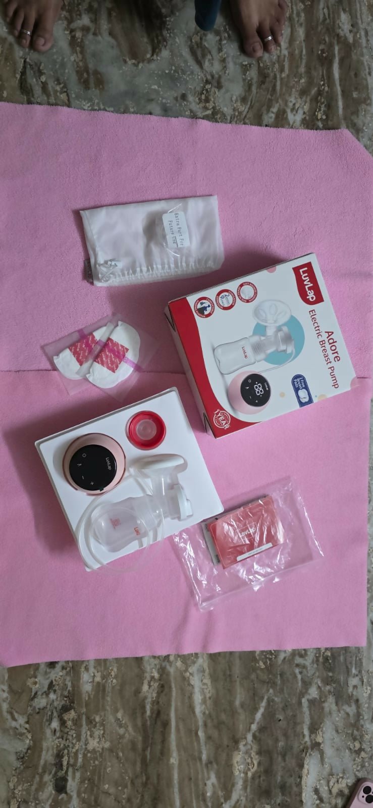 Baby care products including a bottle, wipes, and other items on a pink surface.