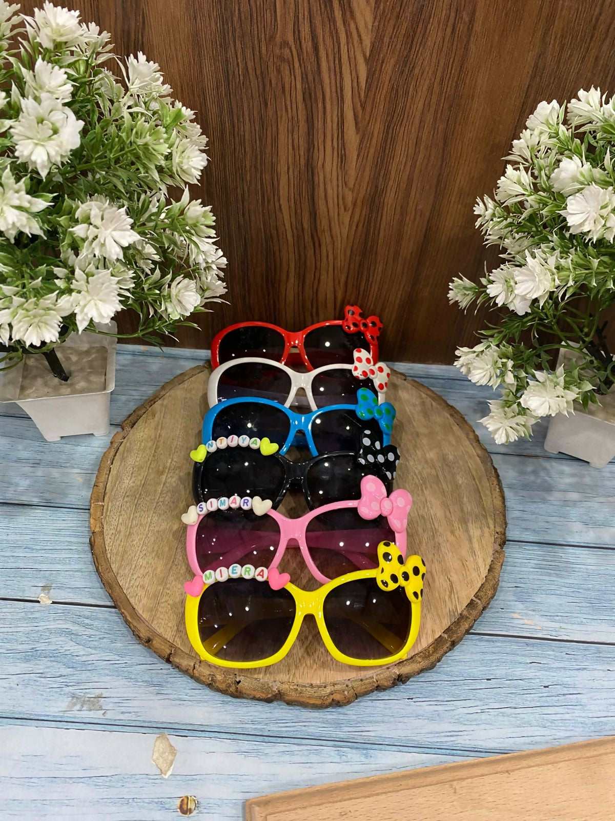 Colorful sunglasses with decorative elements on a wooden stand with flowers in the background