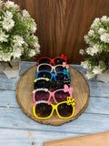 Colorful sunglasses with decorative elements on a wooden stand with flowers in the background