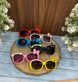 Colorful children's sunglasses with decorative elements on a wooden board.
