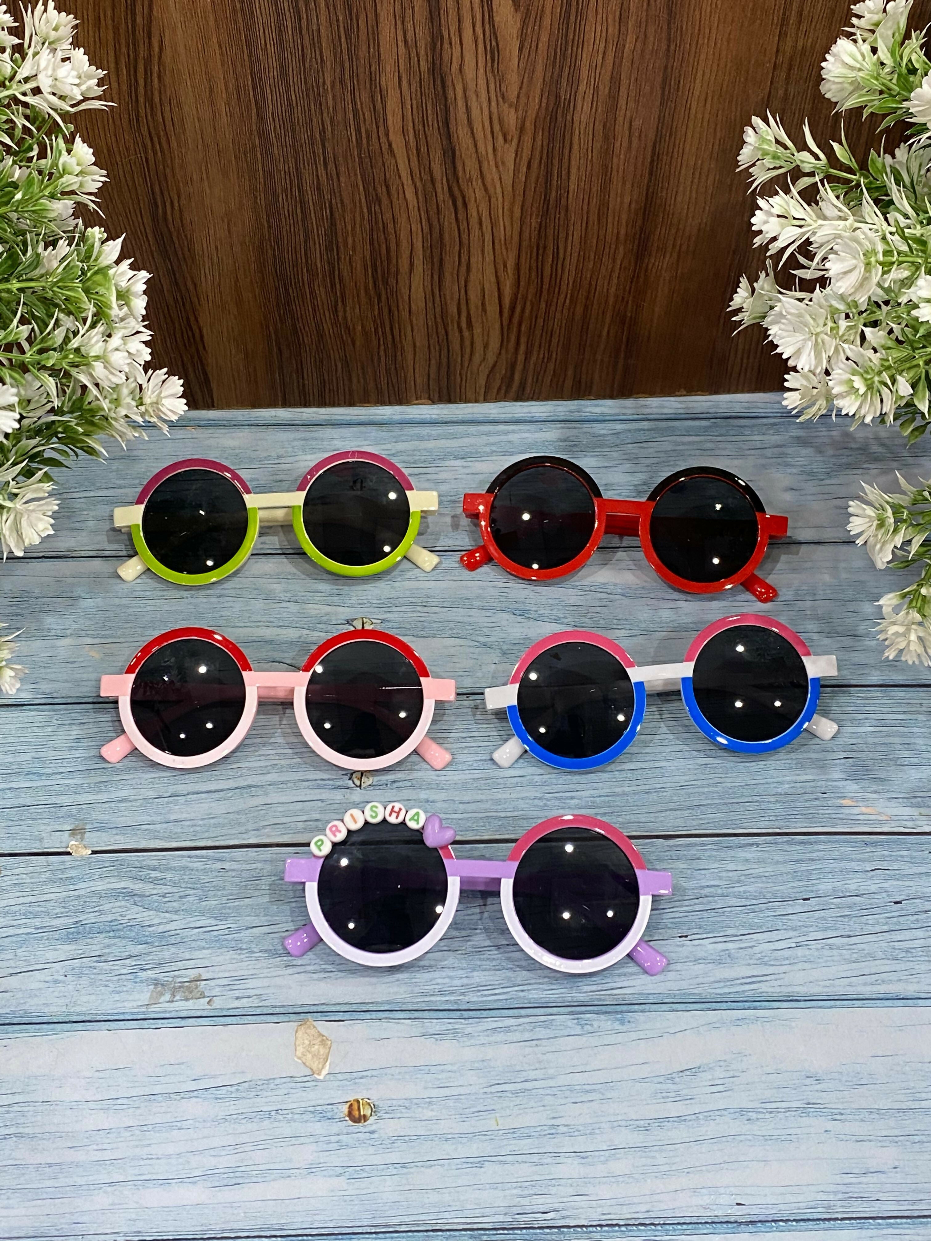 Set of colorful children's sunglasses on a wooden surface with flowers.