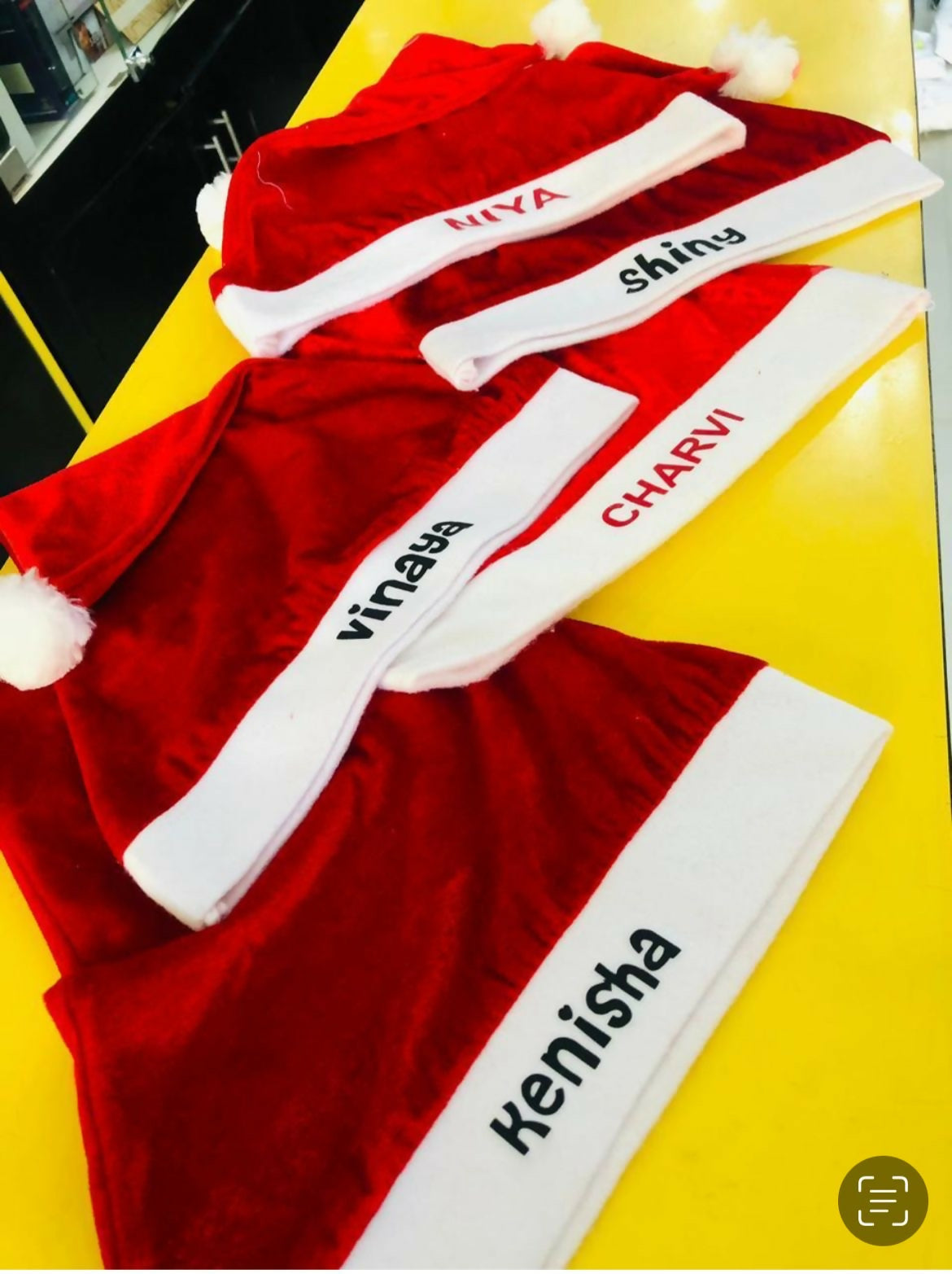Red Santa hats with white bands featuring names on a yellow surface