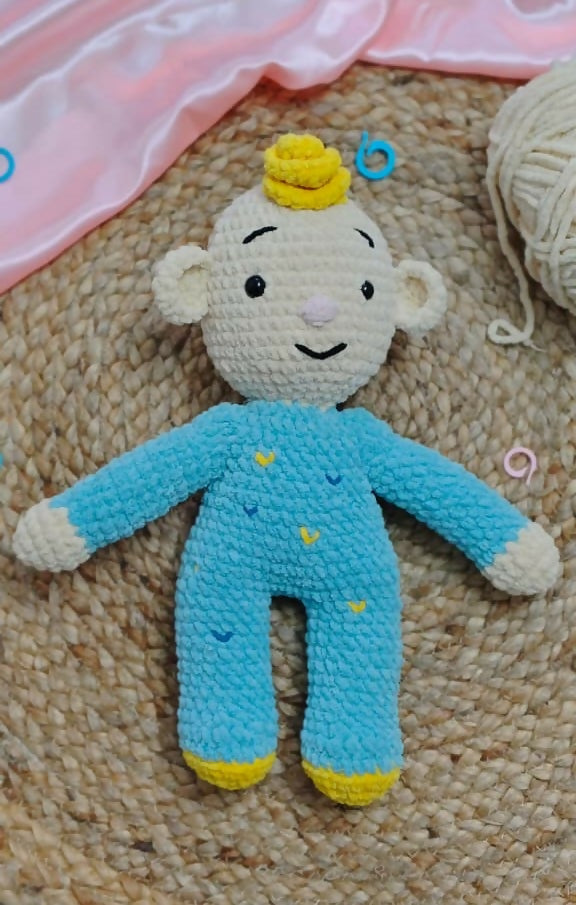 Crocheted toy with blue outfit and yellow accents on a textured surface