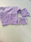Purple knitted baby outfit with a hat on a light gray background