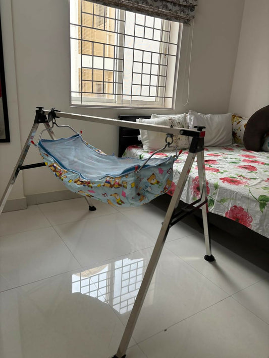 Baby hammock with floral design on a stand in a room with a bed and window.