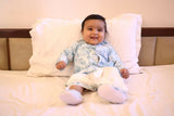 Baby sitting on a bed wearing a patterned outfit.