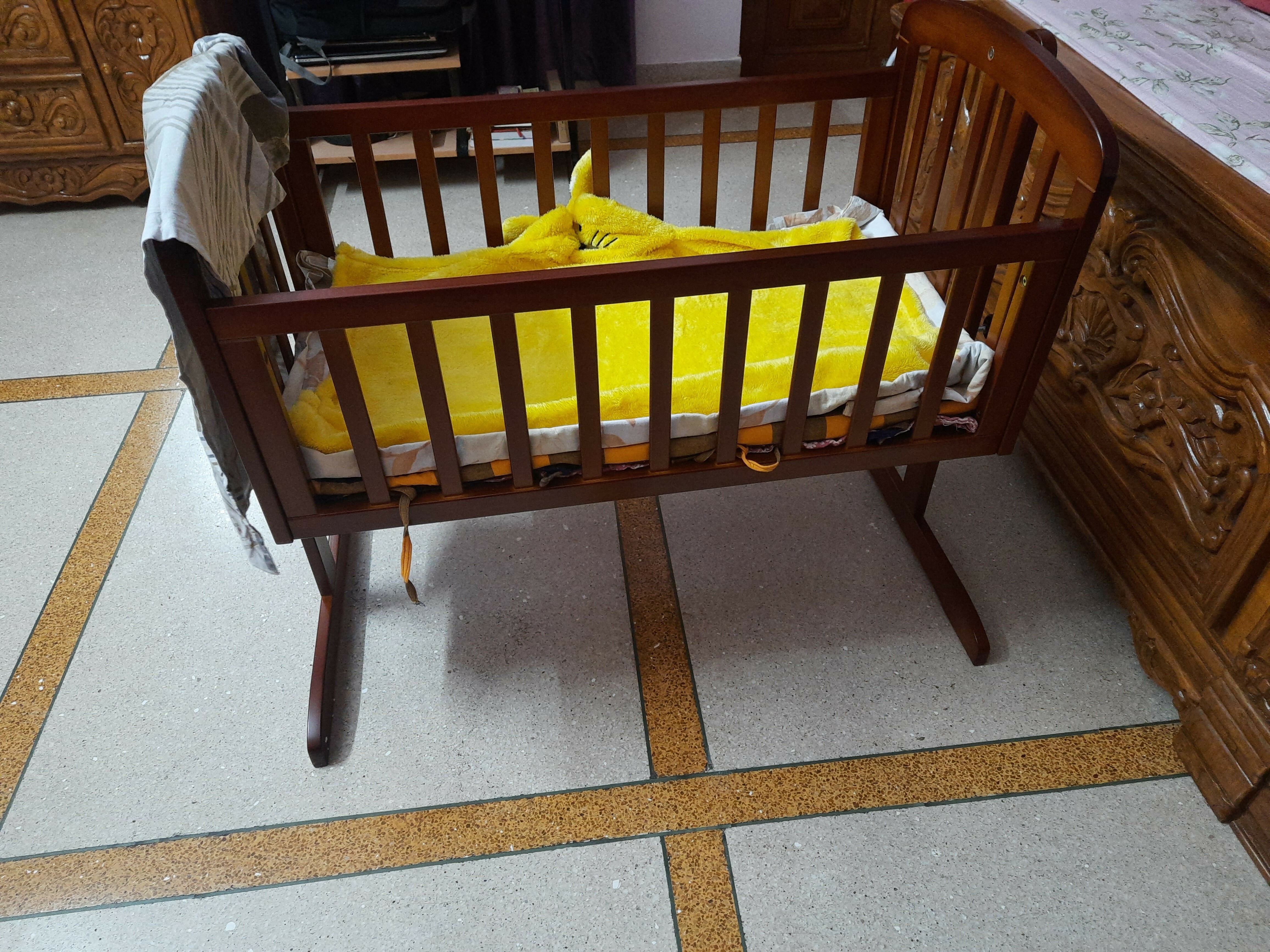 Wooden cradle with yellow mattress on a tiled floor