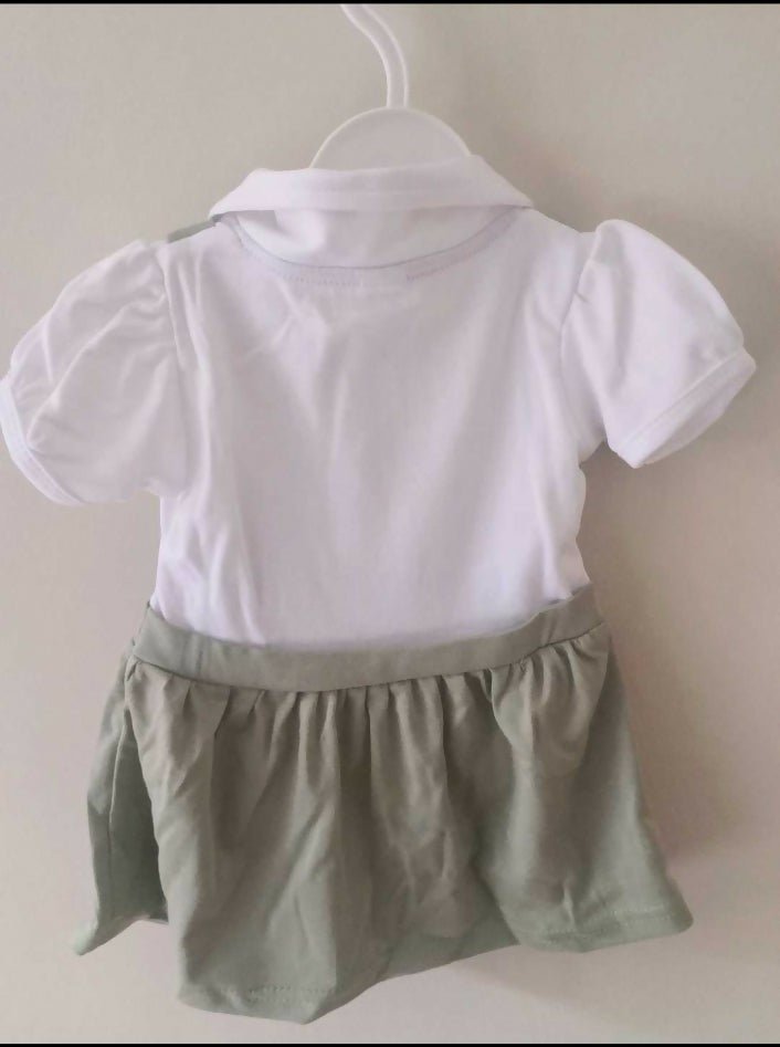 White shirt and green shorts set on a hanger against a plain background