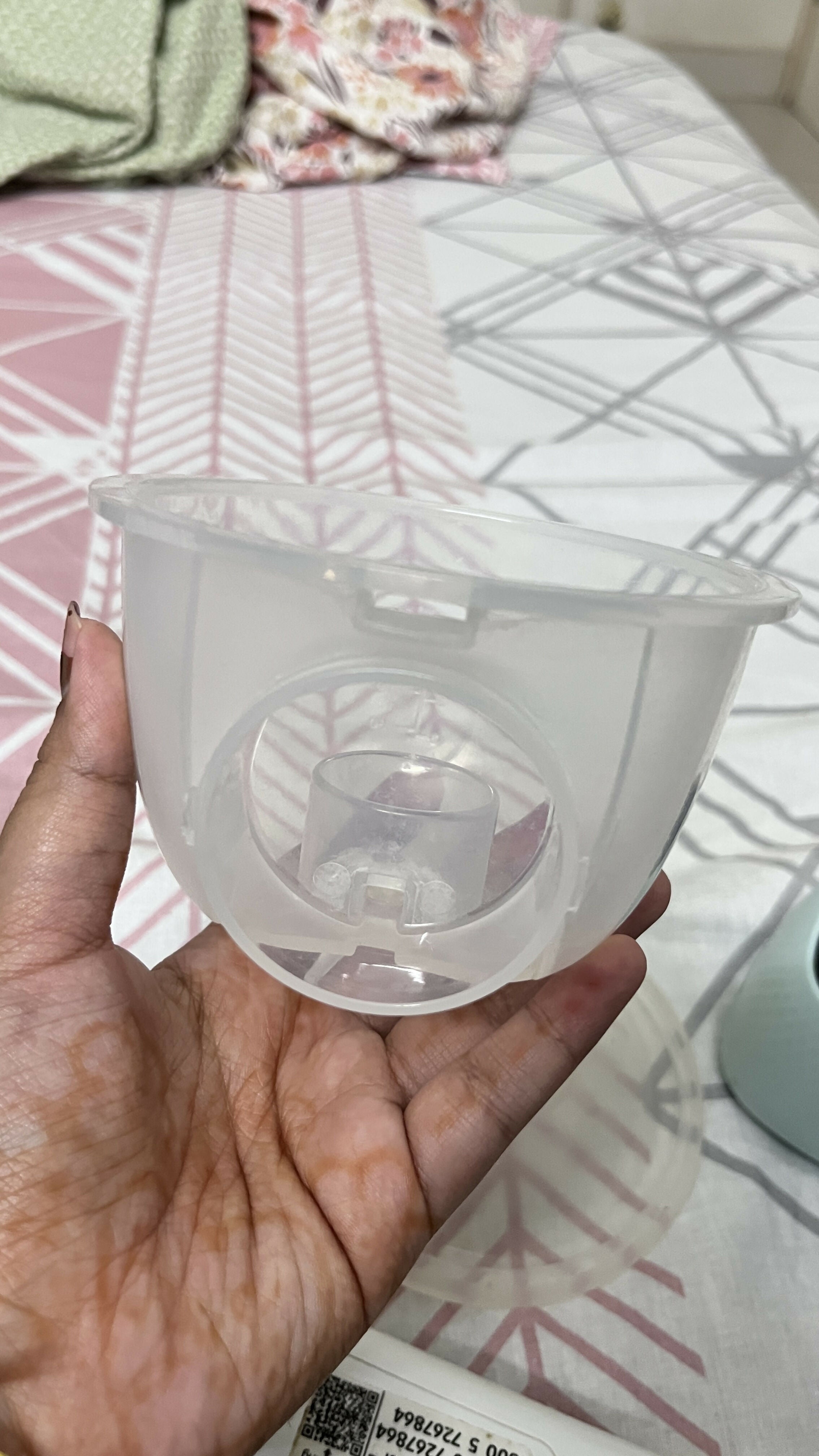 Hand holding a clear plastic container with a white object inside on a patterned surface.