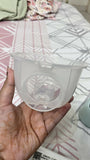 Hand holding a clear plastic container with a white object inside on a patterned surface.