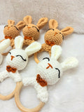 Set of crochet bunny rattle toys with wooden rings on a soft surface
