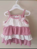 Pink and white baby dress on a hanger against a plain background