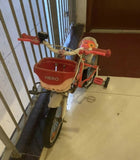 Child's bicycle with a red basket labeled 'Hero' indoors.